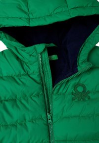 Grüne gepolsterte Jacke mit Kapuze, teilweise aufgezogen, um das dunkle Fleece-Innenfutter und das gestickte Logo auf der Brust zu zeigen.