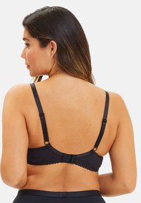 Sujeción negra con ribete de encaje, tirantes ajustables y cierre de gancho y ojo. Hecha de un material suave, con un brillo sutil.