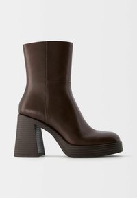 Botte en cuir mi-mollet marron foncé avec un bout arrondi, un talon épais à bloc et une semelle compensée sur un fond clair uni.