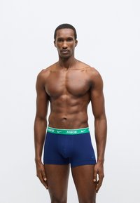 Tmavomodré boxerky so zeleným pásom Nike, ktoré majú priliehavý strih a jemnú látku. Pás obsahuje logo Nike v bielej farbe.