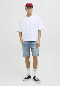 Hvid kortærmet T-shirt, lys blå denimshorts, rød kasket med logo, sorte sneakers og hvide sokker med branding. Afslappet outfitdesign.