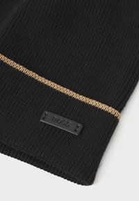 Sort strikhue med en tekstureret overflade, prydet med en kontrasterende gul stribe og et sort prægede logo-label. Fremstillet af blødt, fleksibelt materiale.