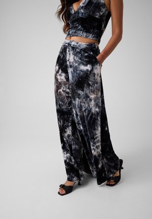 Femme portant un pantalon large tie-dye noir et blanc, un top court assorti et des sandales noires à talons avec un nœud.