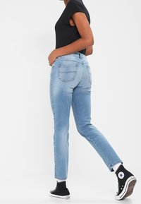 Ljusblå denimjeans med slim fit, med bakfickor och en lätt blekning. Matchas med en svart topp med kort ärm och svarta sneakers.