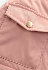 Nærbillede af en pink stoflomme med en klap, der er sikret med en rund gylden knap og synligt syning langs sømkanten.