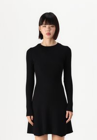 Robes en tricot noir avec des manches longues, texture côtelée, corsage ajusté et jupe évasée. Encolure ronde et design sans coutures. Pas de matériel visible.
