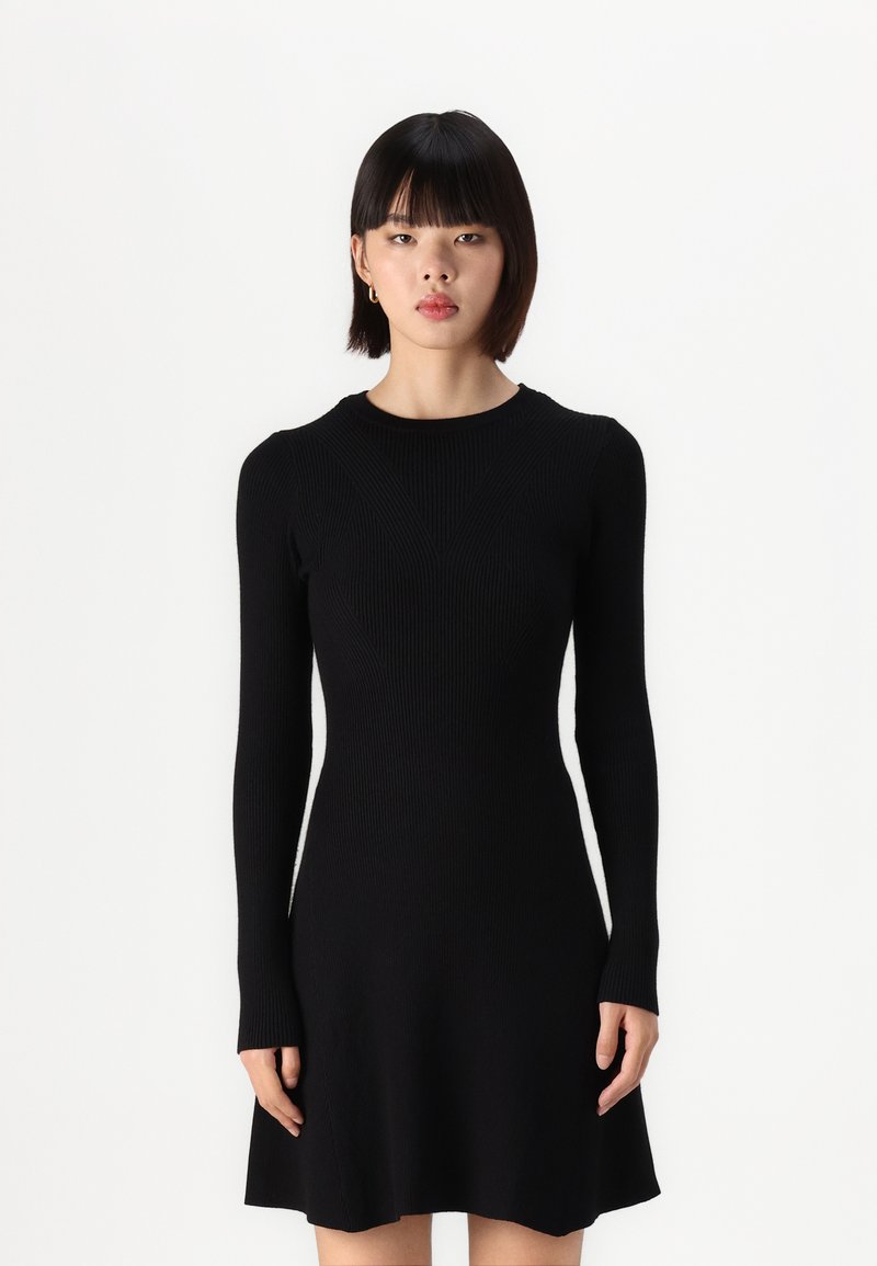 Robes en tricot noir avec des manches longues, texture côtelée, corsage ajusté et jupe évasée. Encolure ronde et design sans coutures. Pas de matériel visible.