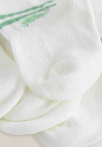 Calze di cotone bianche con texture a coste, dotate di strisce verdi e un design a foglia. Tessuto morbido e leggero, ideale per l'uso quotidiano.
