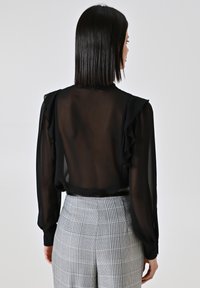 Blusa nera trasparente con spalle voluminose e maniche lunghe. Abbinata a pantaloni a vita alta grigi a quadri con un motivo a scacchi.