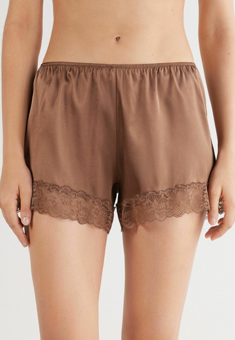 Bruna satinshorts med resårem i midjan, med en scalloped spetsdetalj vid fållen. Slät textur och avslappnad passform.