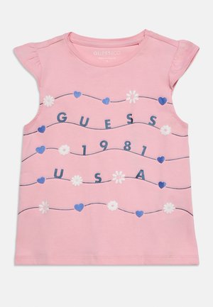 Roosa varrukateta väikelapse särk siniste südamete, valgete lillede ja laineliste joontega valgel tekst "GUESS 1981 USA" ees.