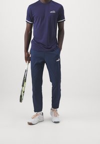 Námořnický sportovní outfit obsahující tričko s krátkým rukávem a bílými lemy, spolu s odpovídajícími kalhotami s červenými akcenty. Tenisky v bílé a světle růžové barvě.