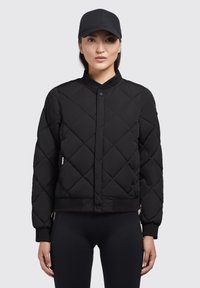 Zwarte gewatteerde bomberjack met een ronde kraag, drukknopen aan de voorkant en ribgebreide manchetten. Draagt over zwarte leggings, met een zijlogo-label.