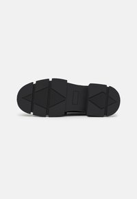 Talpă de pantof neagră cu o suprafață din cauciuc texturat, având un design segmentat și modele geometrice pentru o aderență și stabilitate sporită.