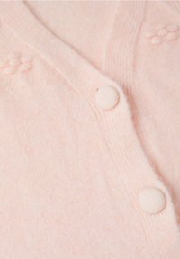 Tissu en maille rose doux avec deux boutons ronds recouverts de tissu et un détail subtil de points en relief près de l'encolure.