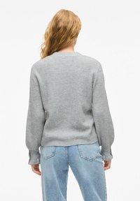 Siv pleten jumper z rebrasto teksturo, okroglo ovratnikom in dolgimi rokavi. Združen s svetlo modrimi denim hlačami.