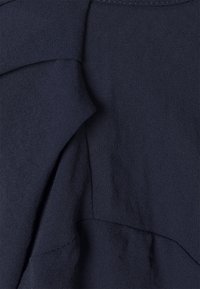 Tessuto blu navy con una superficie liscia, caratterizzato da elementi di design stratificati e dettagli di cucitura sottili. Nessun motivo o accessorio visibile.
