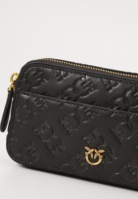 Melnas reljefā ādas maku ar rāvējslēdzēja aizdari, ar teksturētu ziedu rakstu un zelta krāsas logotipa akcentu priekšpusē.