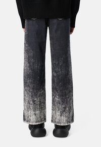 Jeans de pierna ancha confeccionados en denim con un degradado de negro a blanco desgastado. Con dobladillos sin rematar y una superficie texturizada. Combinados con zapatos negros.