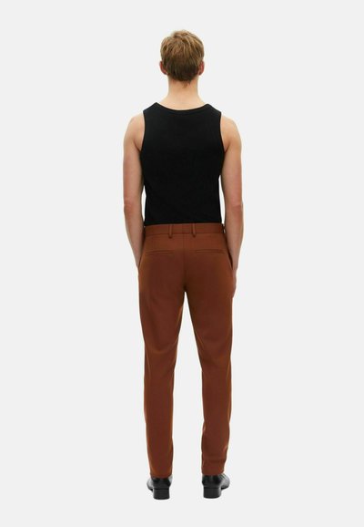 Sort ærmeløs tanktop parret med brune bukser. Bukserne har en glat tekstur, skræddersyet pasform og to baglommer.
