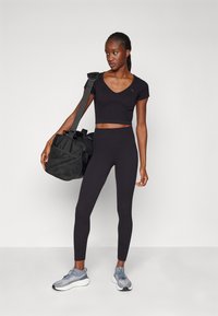 Top crop sportivo nero e leggings, realizzati in tessuto elasticizzato. Presenta un scollo a V, design testurizzato, con uno zaino e sneakers grigie.
