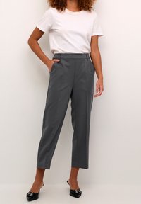 Pantalons gris ajustés avec une taille plate, poches latérales et une coupe fuselée, associés à un t-shirt blanc uni et des mules noires.