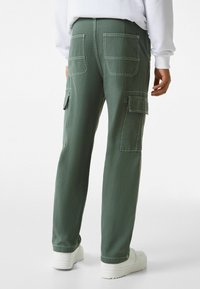 Zelené cargo kalhoty vyrobené z bavlny, s dvěma zadními kapsami a bočními cargo kapsami. Design zahrnuje kontrastní švy a zúžený střih.