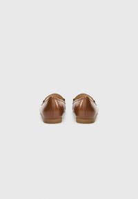 Ballerines en cuir marron avec un bout arrondi, une semelle plate, et un détail de couture à l'arrière. Design minimaliste, texture lisse.