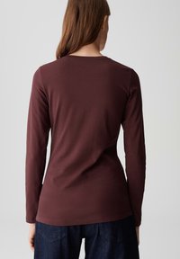 Langarmtop in donker bordeaux katoen. Heeft een ronde halslijn en een aansluitende pasvorm, met een gladde, zachte textuur.