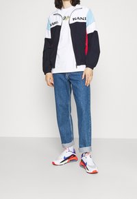 Urheilullinen laivastonsininen takki vaaleansinisin, punaisin ja valkoisin yksityiskohdin. Yhdistetty valkoiseen t-paitaan, rentoihin sinisiin farkkuihin ja monivärisiin lenkkareihin.