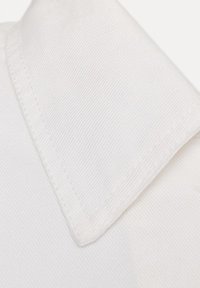 Valge kangase krae lähivõte, kus on nähtavad õmblused ja diagonaalse triibulise tekstuuriga muster, rõhutades õmblust ja nurga detaili.