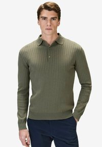 Olivgrön ribbad långärmad polo med krage, med en knappslå och en åtsittande silhuett. Texturerad stickad tyg.