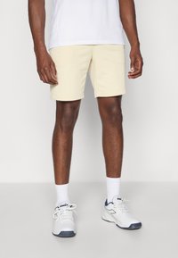 Cremfarbene Shorts aus einem weichen Stoff mit elastischem Bund, kombiniert mit weißen Sneakers und gerippten weißen Socken.