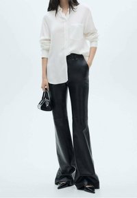 Witte, lange mouwen blouse met een borstzak, gedragen met hoge zwarte leren flared broek en een kleine zwarte handtas.