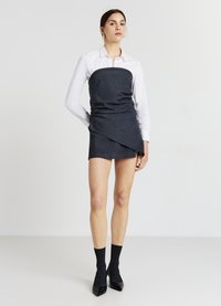 Abito mini plissettato grigio scuro con corpetto aderente, design a strati e una camicia bianca colletto sotto. Scarpe nere con tacco alto e calze.