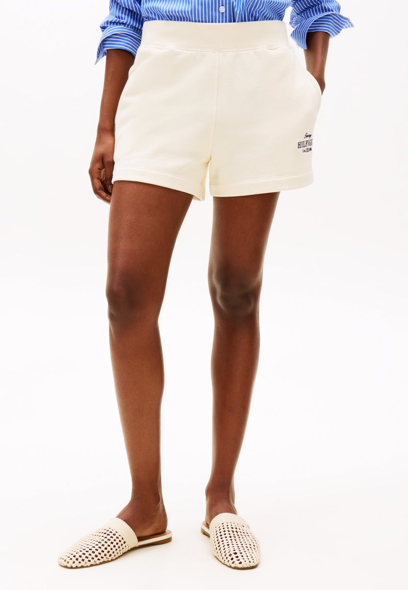 Cremefarvede atletikshorts med en glat tekstur, der har sidelommer og et trykt logo. Parret med vævede beige slip-on sko.
