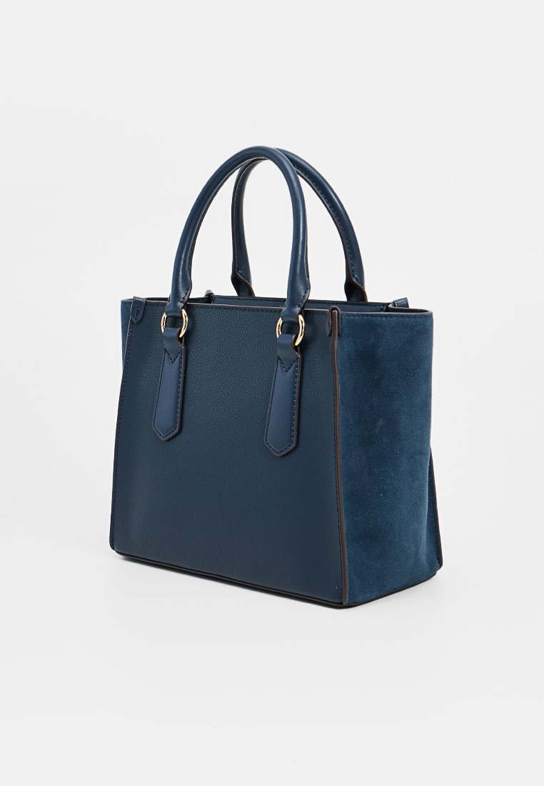 Borsa strutturata di colore blu navy con doppi manici superiori, parte anteriore in pelle testurizzata e pannelli laterali in suede su uno sfondo bianco.
