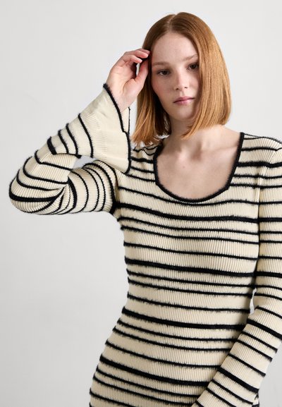 Striped ribbed sweater in cream and black. Features a scoop neckline and long sleeves with flared cuffs. Soft texture and fitted design.