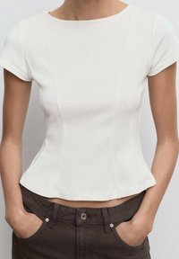 Biely priliehavý top s krátkymi rukávmi, ribbovanou textúrou a peplum lemom. Spárovaný s tmavohnedými nohavicami s detailom kovových gombíkov.