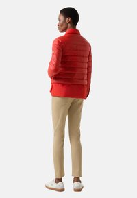 Rote Steppjacke mit hohem Kragen, kombiniert mit beigen Hosen und weißen Sneakern mit brauner Sohle.