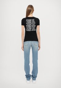 T-shirt nera a maniche corte con testo bianco sul retro. Abbinata a jeans di jeans leggeri blu chiaro e sneakers bianche. Tessuto morbido, design aderente.