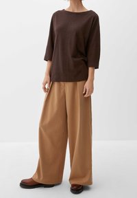 Bruine, losse top met driekwartmouwen, gecombineerd met wijde, lichtbruine broek en donkerbruine schoenen met een gestructureerde zool.