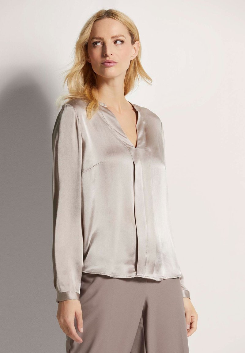 Zijden blouse in lichtgrijs met een V-hals en lange mouwen. Heeft een gladde textuur, subtiele glans en een ontspannen pasvorm.