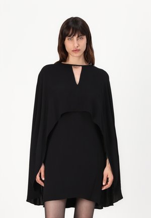 Fekete köpenydressz V-nyakkivágással, folyó anyaggal és rétegezett dizájnnal, amely a könyökökig terjed, drámai sziluettet teremtve.