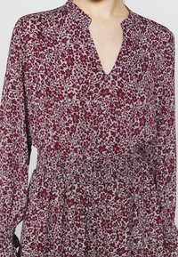 Bordeaux-mönstrad klänning med blommor, V-ringning, långa ärmar och elastisk midja. Lättviktig tyg med intrikata, små blommönster.