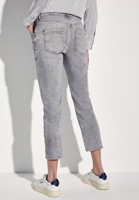 Gray cropped jeans with a faded texture, five pockets, and a straight-leg design, paired with white sneakers featuring navy accents.