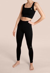 Schwarzes, geripptes Sportset mit einem verkürzten Tanktop mit breiten Trägern und hochgeschnittenen Leggings, beide mit kleinen Logo-Akzenten.