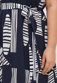 Vestido de color marino con patrones abstractos en blanco; presenta un cinturón atado en la cintura y tela texturizada; los colores contrastan de manera contundente para un diseño audaz.