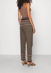 Brun tanktop i kombination med mönstrade bruna och svarta tapered byxor med en texturerad design och randig midja. Stiletto-sandaler.