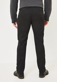 Schwarze Hosen mit geradem Schnitt, subtiler Textur, zwei Gesäßtaschen mit Knöpfen, kombiniert mit dunklen Schuhen und einem grauen Strickpullover.